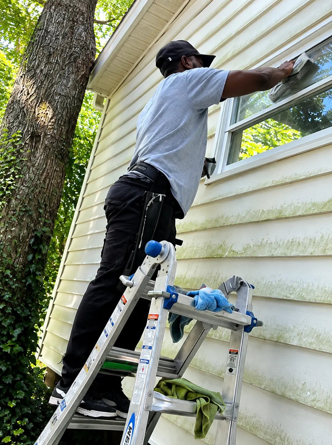 Technician cleaning second-story windows from a ladder